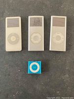 Front view of 3 white Apple iPods with click wheels and 1 blue iPod Shuffle, showing condition and form factor.