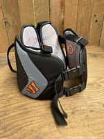 Side view of black and grey Warrior lacrosse kidney pads showing outer fabric and straps.
