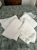 Four white sheer curtain panels folded and placed on a bed with a gray textured blanket.