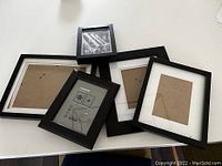 Photo of four black picture frames laid flat on a white surface, showing different sizes and styles including with and without white matting.