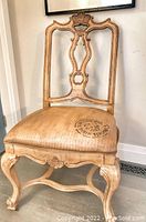 Front view of one wooden dining chair showing ornate carved back and upholstered seat with painted faux leather finish.