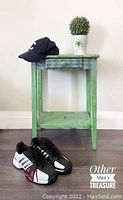 Full view of small green wooden table with a drawer and lower shelf, showing golf-themed elements. The table is painted green with a distressed finish. There is a black cap and a potted plant on top, which are not included in the lot.