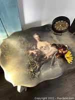 Close-up of table top showing decoupage design of a classical portrait and golden ornamental details.