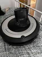 Black iRobot Roomba robotic vacuum cleaner with top charging dock visible, placed on gray carpet.