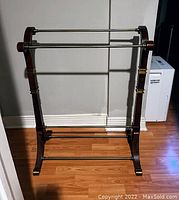 Full view of quilt and blanket hanger showing dark wood frame, three metal horizontal rods, and curved legs.