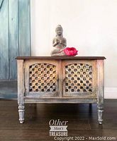 Front view of the boho style side table showing stained wood top, painted lattice doors, and turned legs.