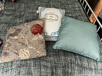 Three throw cushions of different sizes and designs arranged on a dark textured surface.