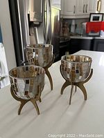 Photo of three mosaic glass tea candle holders with metal stands arranged on kitchen counter.