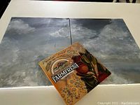 Three canvases laid flat showing two cloudy sky paintings and one small farm fresh mixed media artwork