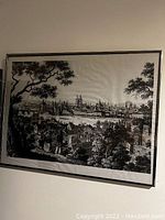 Framed black and white cityscape print on cloth showing a large historic city with multiple buildings and trees in foreground.