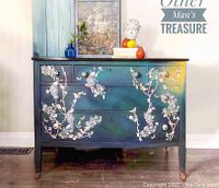 Front view of painted wooden dresser showing blue-yellow gradient finish, white floral stenciling, three drawers with glass knobs