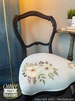 Front view of the vintage parlor chair showing black painted frame and white floral upholstery with painted flowers.
