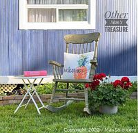 Photo showing an olive green wooden vintage rocking chair with carved details on the top rail, spindle backrest, curved rockers, placed on grass with a pillow for staging.