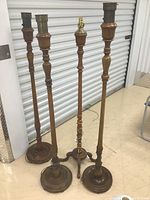 Three tall antique wood floor lamps with turned wooden columns and round wooden bases, metal fittings on top for lamp shades.