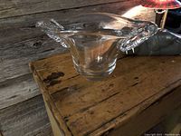 Front angled view of Daum France clear glass vase on wooden surface showing shape and design with curved rim.