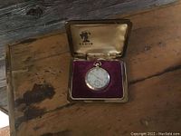 Front view of pocket watch resting in open Elgin presentation case showing dial and box interior logo