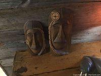 Front and angled view of smaller and larger Delmar Joseph carved wooden masks on rustic wood surface.