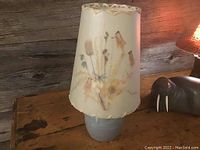 Front view of pottery lamp with floral motif parchment lampshade on wooden table next to a carved walrus figure.
