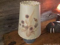 Front view of floral parchment-style lamp shade on blue-gray pottery base.