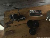 Full view of the Mitchell 300 open-faced fishing reel, spare spool with its container, and instruction manual laid on a wooden surface.