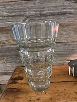 Front-view image of the clear Art Deco glass vase showing its sculptural design, size, and clarity. The wooden background and small walrus figure are visible.