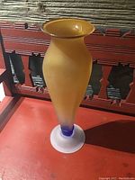 Front view of tall frosted glass vase with amber to purple gradient and frosted base on a decorative red surface.