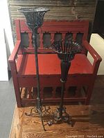 Front view of the two candle holders placed in front of a red bench, showing their height difference and intricate metalwork.