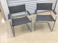 Front angle view of two grey leather chairs with metal frames, showing condition and design.