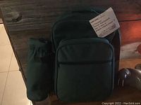 Backpack picnic basket shown from the front with attached bottle holder pouch on side and tag describing the 2 person picnic set.