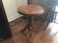 Front angle view of vintage wooden adjustable piano stool showing round seat and three leg base