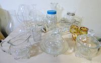 Photo shows a wide variety of clear glass items including lamp globes, drinking glasses, butter dish, and decorative glassware