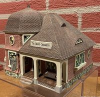 Front and side view of The Grand Creamery collectible building showing the porch with bench and signage.