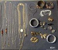 Overview of assorted costume jewelry including necklaces, bracelets, bangles, brooches, and earrings laid out on fabric background.
