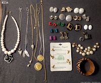 Full lot view showing multiple necklaces, earrings, bracelets, and charms laid out on a dark surface.