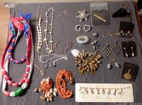 Full lot of mixed costume jewelry including necklaces, earrings, brooches, pins, and bracelets laid out on table