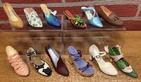Full lot of 12 miniature collectible shoes displayed on clear risers against brick background.