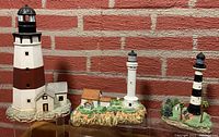 Three lighthouse figurines on clear stands in front of brick wall: Montauk Point (left), Harbour Lights Point Arena (center), Harbour Lights Cape Canaveral (right)