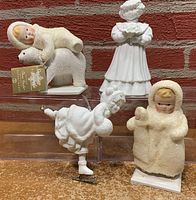 Four figurines displayed including a Snow Angels figure resting on a polar bear, a child in winter coat, and two Silhouette Treasures figures including an ice skater and a figure holding an item.