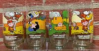 Photo shows front views of 4 glasses with colorful Camp Snoopy Collection characters and camp themed backgrounds.