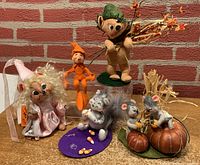 Full lot view showing all 5 Annalee doll items arranged on a table with brick background, including the pink dress doll, mouse dolls on pumpkins, small orange elf, and larger green hat doll.