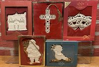 Lot of five Lenox porcelain ornaments in original boxes against a brick background. Includes Toy Shoppe house, cross, holly design, Santa with metal sack, and teddy on sled.