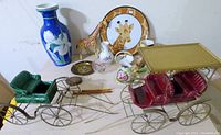Wide shot showing all lot items on table including two Metlox carriage figurines, Bauscher Weiden vase, giraffe toys, and multiple small ceramic vases and plates.