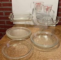 Photo showing all 10 Pyrex pieces including measuring cups, pie pans, bakeware, and glass lid displayed on stands and flat surface.