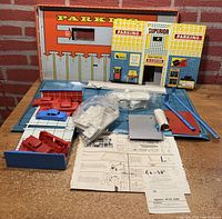 View of many components including a blue plastic base with ramps, several white plastic and steel panels, a small blue plastic car, and original instructions.