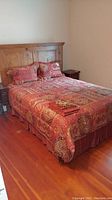Queen size bed made up with red and gold patterned comforter, pillow shams, and bed skirt in a bedroom corner.