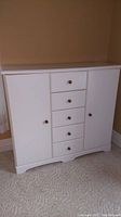 Front view of a white wooden dresser with five drawers in the center and two doors on the sides featuring round wooden knobs.
