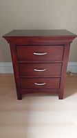 Front view of the wooden three drawer nightstand showing silver handles and overall shape.