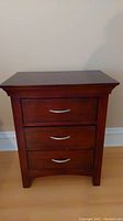 Front view of wooden nightstand with three drawers and metal handles