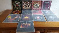 Twelve vinyl records by The Cult arranged on wooden table, mix of LPs and singles