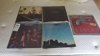 Overview photo showing five Eagles vinyl LP albums on mattress, covers visible, including Eagles Live, The Long Run, and others.
